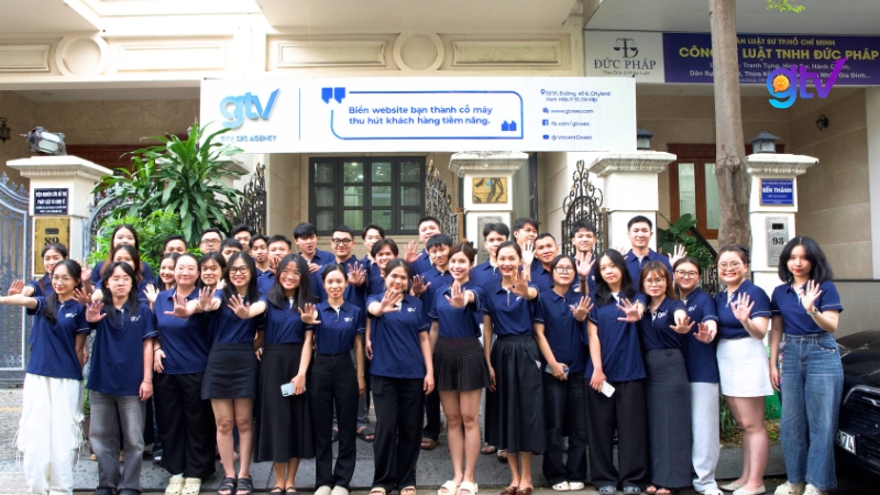 Đội ngũ GTV SEO mặc đồng phục xanh navy chụp ảnh tập thể tại văn phòng, agency triển khai dịch vụ SEO mũ trắng