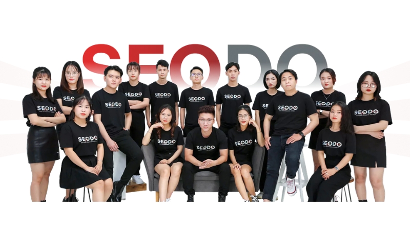 Đội ngũ nhân sự SEODO mặc áo đen in logo chụp ảnh tập thể trước backdrop thương hiệu công ty SEO Branding