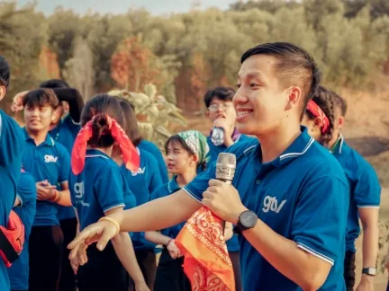 Thành viên GTV SEO cầm micro dẫn trò chơi, xung quanh là đồng nghiệp mặc áo xanh