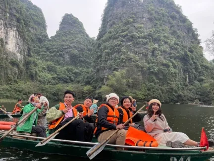 Thành viên GTV SEO mặc áo phao ngồi thuyền nan trên sông, phía sau là núi đá vôi