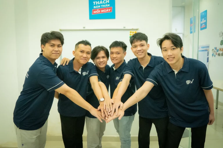 Các thành viên GTV SEO mặc áo polo xanh than đặt tay chồng lên nhau tại văn phòng