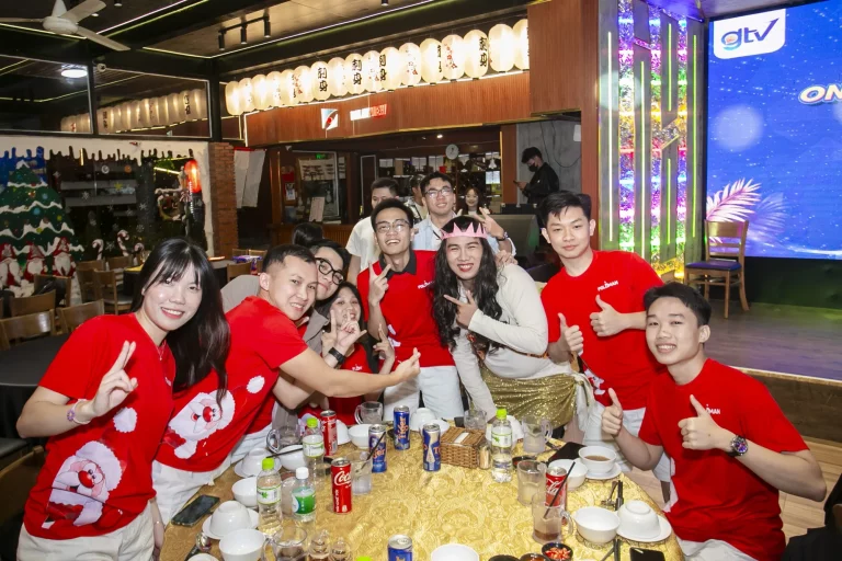 Thành viên GTV SEO mặc áo đỏ in hình ông già Noel giơ tay chào bên bàn tiệc