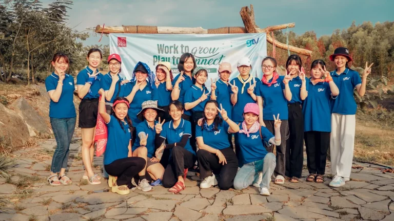 Thành viên GTV SEO mặc áo polo xanh chụp ảnh dưới băng rôn Work to grow, Play to connect